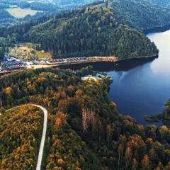 Malownicze jezioro Lubachowskie otoczone lasami. Kręta droga wije się po zboczu, a nad wodą widać zabudowania.