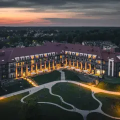 Wieczorny widok na hotel Radisson, z oświetlonymi oknami i tarasami, otoczony zielenią i spokojną okolicą.