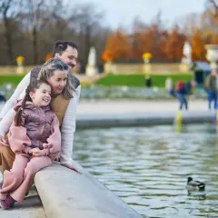Rodzina z córką siedzi nad stawem, obserwując kaczki. Idealne miejsce, gdzie na wakacje z dziećmi, pełne spokoju i piękna.