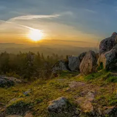 Zachód słońca nad lasem i skalistym szczytem. Miedzianka góra w złotej poświacie, z kamieniami na pierwszym planie.