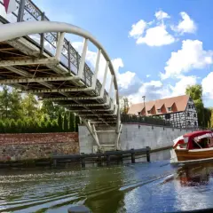 Rejs po Brdzie w Bydgoszczy to idealna propozycja na wycieczki dla seniorów. Drewniana łódź pod nowoczesnym mostem.