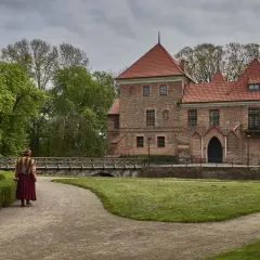 Kobieta w stroju z epoki idzie ścieżką do ceglanego zamku. Idealne miejsce, gdzie na weekend z Warszawy.