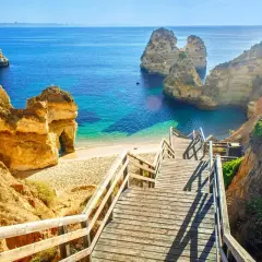 Malownicze klify i turkusowa woda, idealne na portugalia wakacje. Drewniane schody prowadzą na piaszczystą plażę.