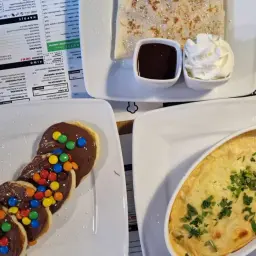 Pankejk menu: słodkie placuszki z czekoladą i kolorowymi drażetkami, obok naleśnik z polewą i bitą śmietaną.