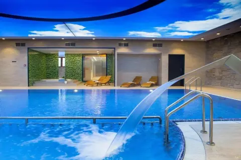 Relaks w hotelu Crocus: basen z wodospadem, leżaki i zielona ściana pod błękitnym niebem.