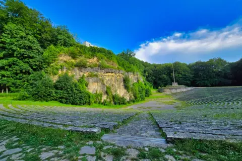 Amfiteatr na Górze Świętej Anny, otoczony zielenią, z kamiennymi ławami i monumentem.