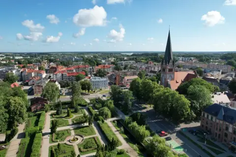 Widok na miasto z wieżą kościelną i parkiem. W oddali widać jezioro. Wieża Bismarcka w Szczecinku nie jest widoczna na tym ujęciu.