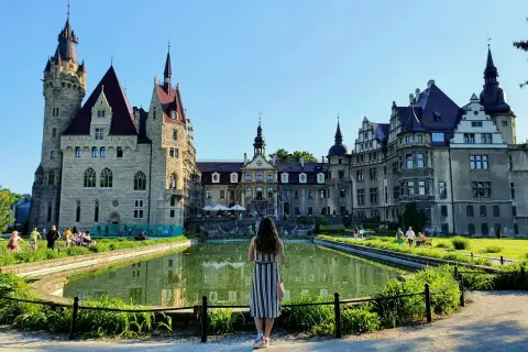 Kobieta podziwia zamek Moszna, jedną z największych atrakcji Opolszczyzny. Wspaniała architektura i staw tworzą magiczny widok.