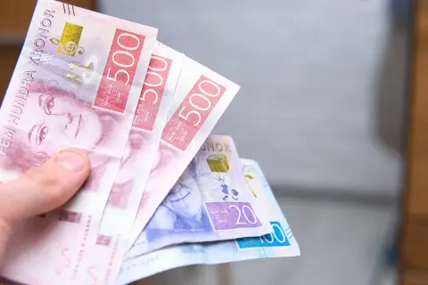 Dłoń trzyma banknoty 500 koron szwedzkich. To właśnie jaka waluta w Szwecji. Widać też banknoty 20 i 100 koron.