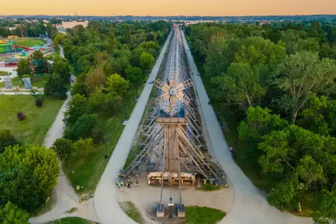 Drewniana konstrukcja tężni solankowej w Ciechocinku, wzdłuż której biegnie ścieżka spacerowa. W oddali park z atrakcjami.