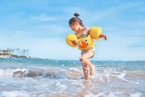 Radosna dziewczynka w żółtym kaczuszce bawi się na plaży. Idealna turcja pogoda maj na wakacje.