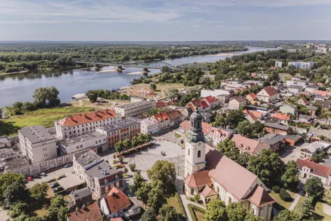 Widok z lotu ptaka na miasto z rzeką i mostem. W centrum plac z kościołem, a w oddali widać zabudowania i las. Na jednym z budynków widoczny napis "Fordon".
