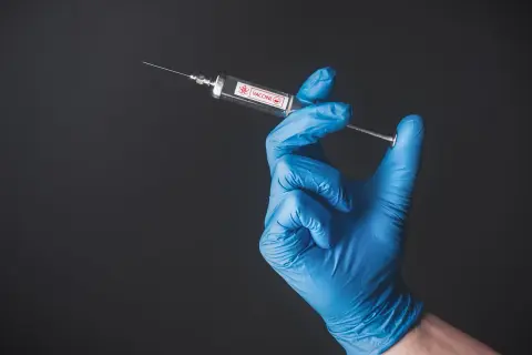 Ręka w niebieskiej rękawiczce trzyma strzykawkę z napisem "VACCINE". Przygotowanie do szczepienia w Tunezji.