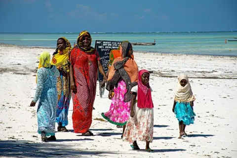 Kobiety i dziewczynki w kolorowych strojach spacerują po plaży. Czy Zanzibar to państwo? To pytanie często zadawane przez turystów.