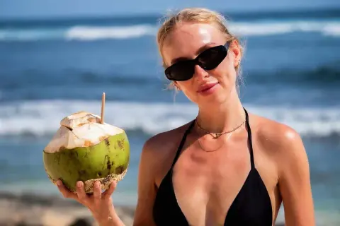 Kobieta w czarnym bikini trzyma kokosa na plaży. Idealne wakacje na Bali z orzeźwiającym napojem.