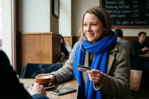 Kobieta z niebieskim szalem płaci kartą w kawiarni. Czy w Norwegii można płacić euro? Nie, Norwegia ma własną walutę.