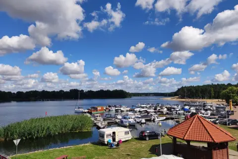 Letni dzień nad jeziorem w Koninie. Port pełen łodzi, przy brzegu kampery i zielona trawa.