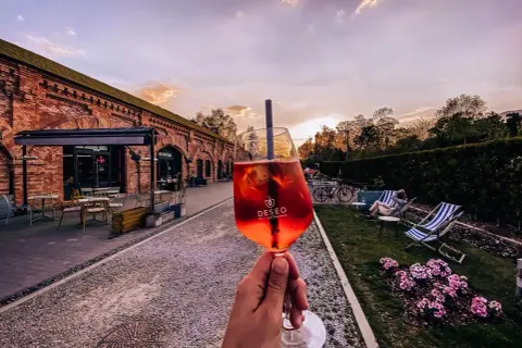 Nietypowe restauracje Warszawa: drink w ręce, ceglany budynek i ogród z leżakami. Idealne miejsce na relaks.