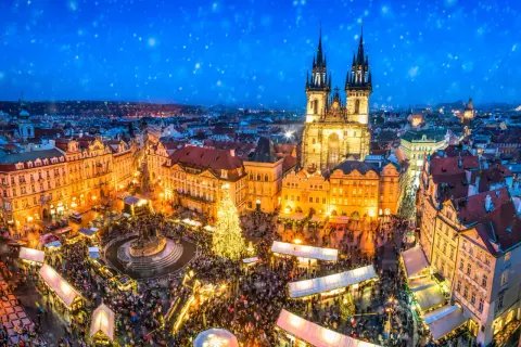 Tłoczny jarmark bożonarodzeniowy na Rynku Staromiejskim w Pradze. Śnieg prószy nad oświetloną choinką i tłumami ludzi. To magiczne święta w Czechach.