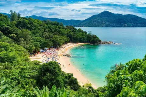 Rajska plaża Kata Beach z turkusową wodą, zielonymi wzgórzami i mnóstwem kolorowych parasoli.