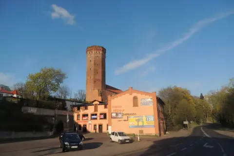 Wieża w Kamieniu Krajeńskim góruje nad budynkami z pizzerią i sklepem.
