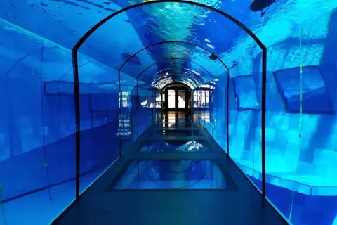 Niebieski tunel z przeszklonym dnem, przypominający spacer pod wodą. Wrażenie jakbyśmy byli w Mszczonowie, ale pod taflą wody.