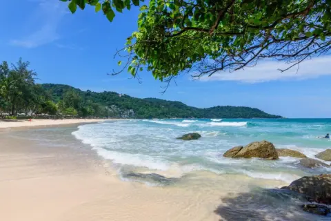 Piękna plaża Kata Beach Phuket z turkusową wodą, falami i zielonymi wzgórzami w tle. Idealne miejsce na relaks.