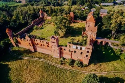 Ruiny zamku w Szymbarku, otoczone zielenią, z charakterystycznymi ceglanymi murami i wieżami.