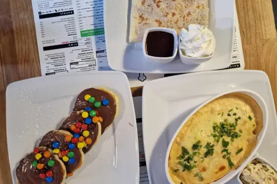 Pankejk menu: słodkie placuszki z czekoladą i kolorowymi drażetkami, obok naleśnik z polewą i bitą śmietaną.