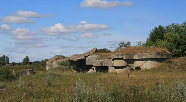 Ruiny fortu Osowiec, betonowe bunkry porośnięte trawą, na tle błękitnego nieba z chmurami.