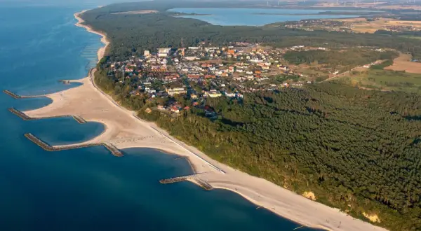 Jarosławiec: widok z lotu ptaka na plażę z falochronami, las i zabudowania.