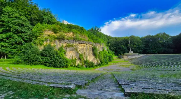 Amfiteatr na Górze Świętej Anny, otoczony zielenią, z kamiennymi ławami i monumentem.