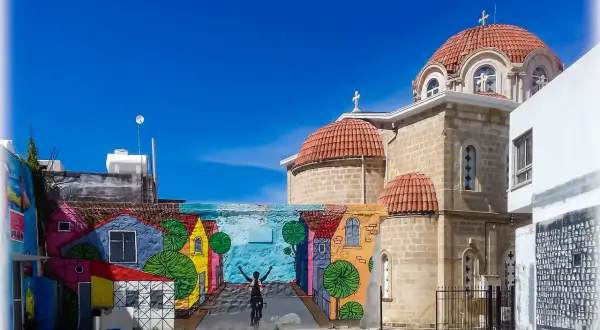 Kolorowy mural z rowerzystą i domkami na tle kościoła z kopułami. Pafos stare miasto.