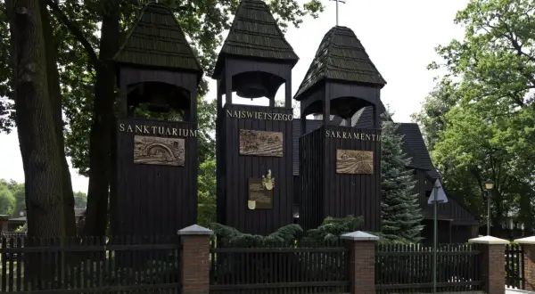 Trzy drewniane dzwonnice przed kościołem w Jankowicach. Na jednej z nich widnieje napis "Sanktuarium Najświętszego Sakramentu".