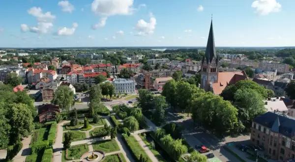 Widok na miasto z wieżą kościelną i parkiem. W oddali widać jezioro. Wieża Bismarcka w Szczecinku nie jest widoczna na tym ujęciu.