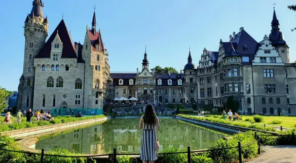 Kobieta podziwia zamek Moszna, jedną z największych atrakcji Opolszczyzny. Wspaniała architektura i staw tworzą magiczny widok.