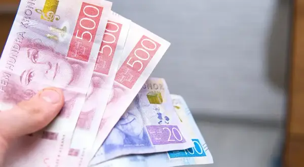 Dłoń trzyma banknoty 500 koron szwedzkich. To właśnie jaka waluta w Szwecji. Widać też banknoty 20 i 100 koron.