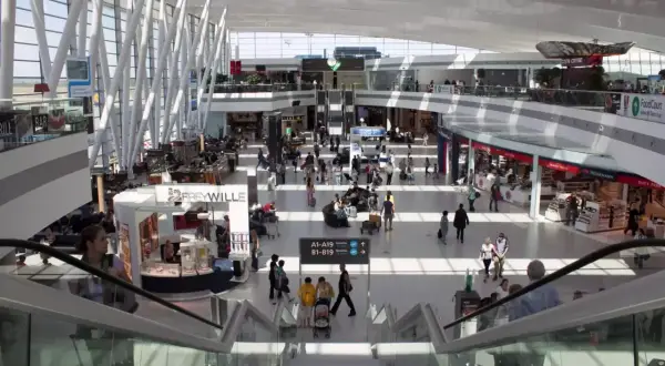 Tętniący życiem terminal lotniska w Budapeszcie. Pasażerowie przemieszczają się między sklepami i kawiarniami, a nowoczesna architektura tworzy przestronne wnętrze.