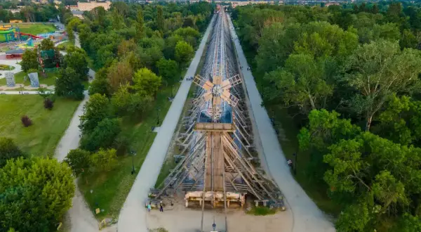 Drewniana konstrukcja tężni solankowej w Ciechocinku, wzdłuż której biegnie ścieżka spacerowa. W oddali park z atrakcjami.