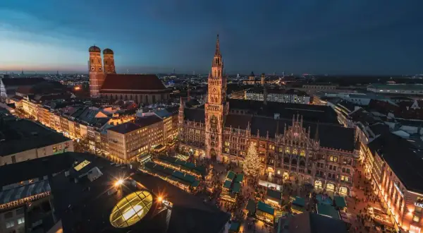 Nocny jarmark bożonarodzeniowy w Monachium. Rynek z oświetlonymi straganami i choinką, w tle majestatyczny ratusz i katedra.