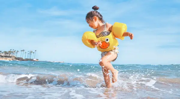 Radosna dziewczynka w żółtym kaczuszce bawi się na plaży. Idealna turcja pogoda maj na wakacje.