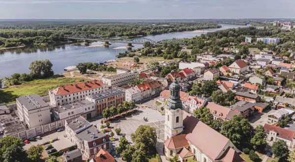 Widok z lotu ptaka na miasto z rzeką i mostem. W centrum plac z kościołem, a w oddali widać zabudowania i las. Na jednym z budynków widoczny napis "Fordon".