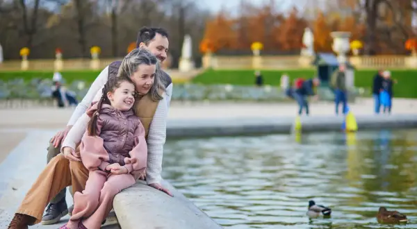 Rodzina z córką siedzi nad stawem, obserwując kaczki. Idealne miejsce, gdzie na wakacje z dziećmi, pełne spokoju i piękna.