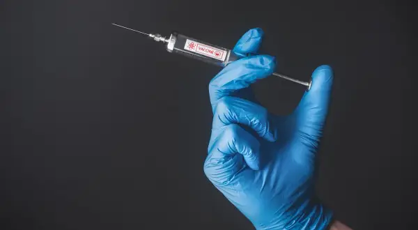 Ręka w niebieskiej rękawiczce trzyma strzykawkę z napisem "VACCINE". Przygotowanie do szczepienia w Tunezji.