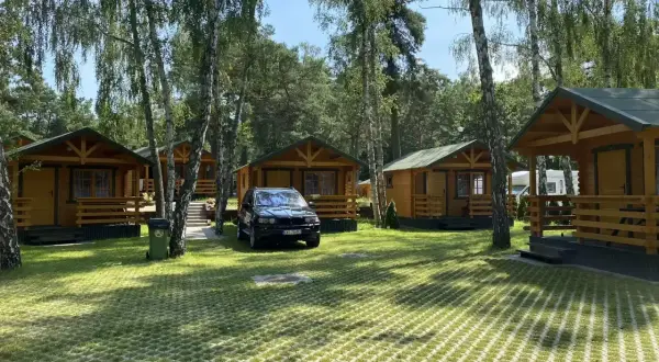 Tanie domki letniskowe nad morzem, otoczone drzewami. Na trawniku stoi czarny SUV.