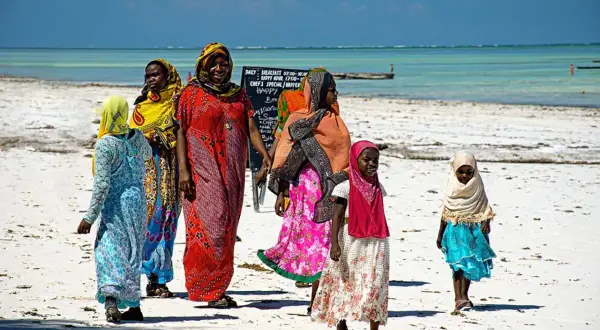Kobiety i dziewczynki w kolorowych strojach spacerują po plaży. Czy Zanzibar to państwo? To pytanie często zadawane przez turystów.