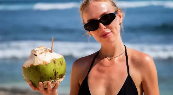 Kobieta w czarnym bikini trzyma kokosa na plaży. Idealne wakacje na Bali z orzeźwiającym napojem.