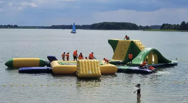 Wodne szaleństwo na Mazurach z dziećmi! Dzieci w kamizelkach ratunkowych bawią się na dmuchanym placu zabaw na jeziorze.