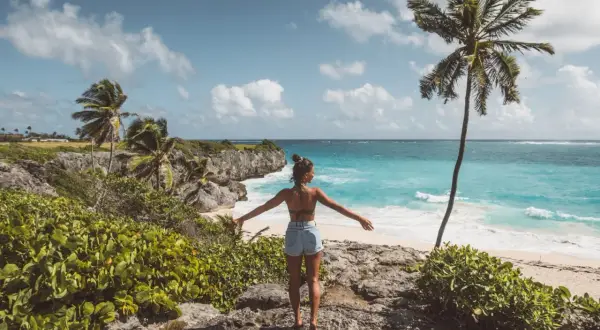 Kobieta z rozłożonymi rękami podziwia turkusowe morze i palmę. Idealne Barbados wakacje.