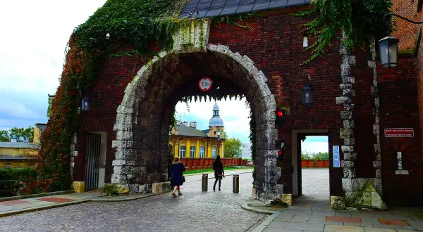 Brama wjazdowa na Wawel, porośnięta bluszczem, zaprasza do zwiedzania. Kamienna konstrukcja i ceglane mury tworzą historyczny klimat.